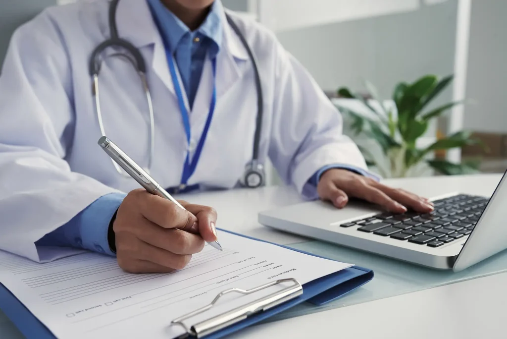 médecin écrivant sur un papier et sur l'ordinateur